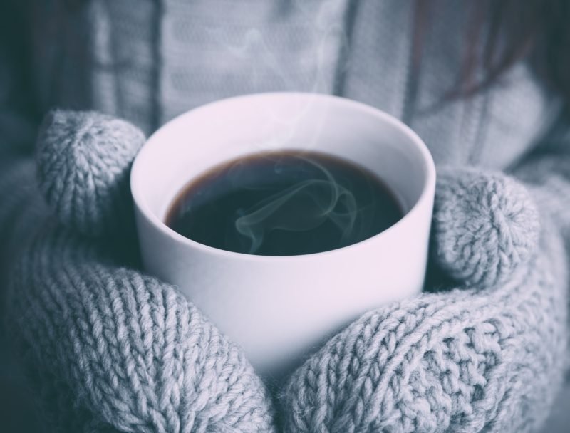 Warm mug of coffee in gloved hands