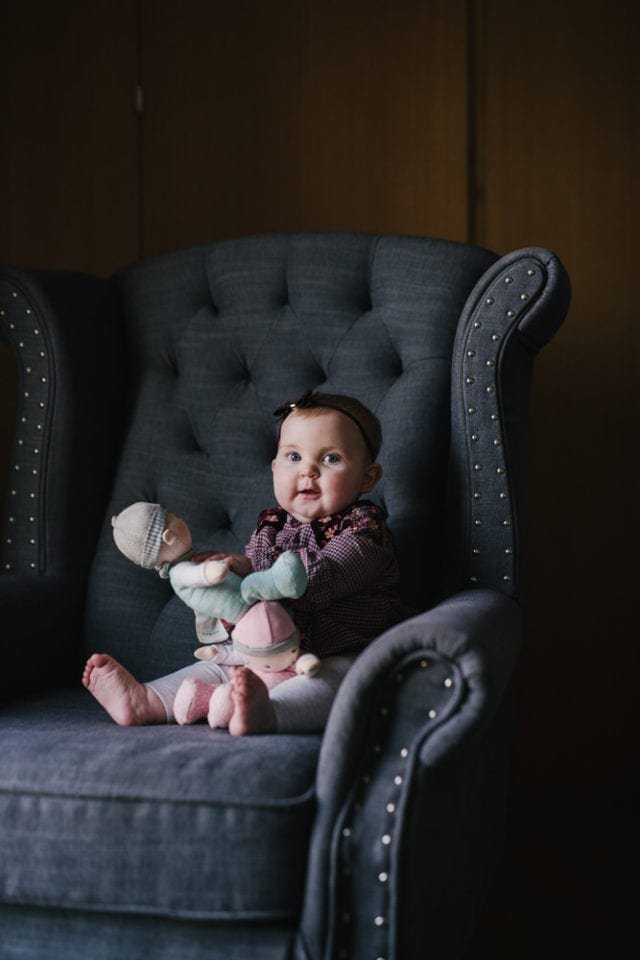 Baby in grey chair with soft baby dolls